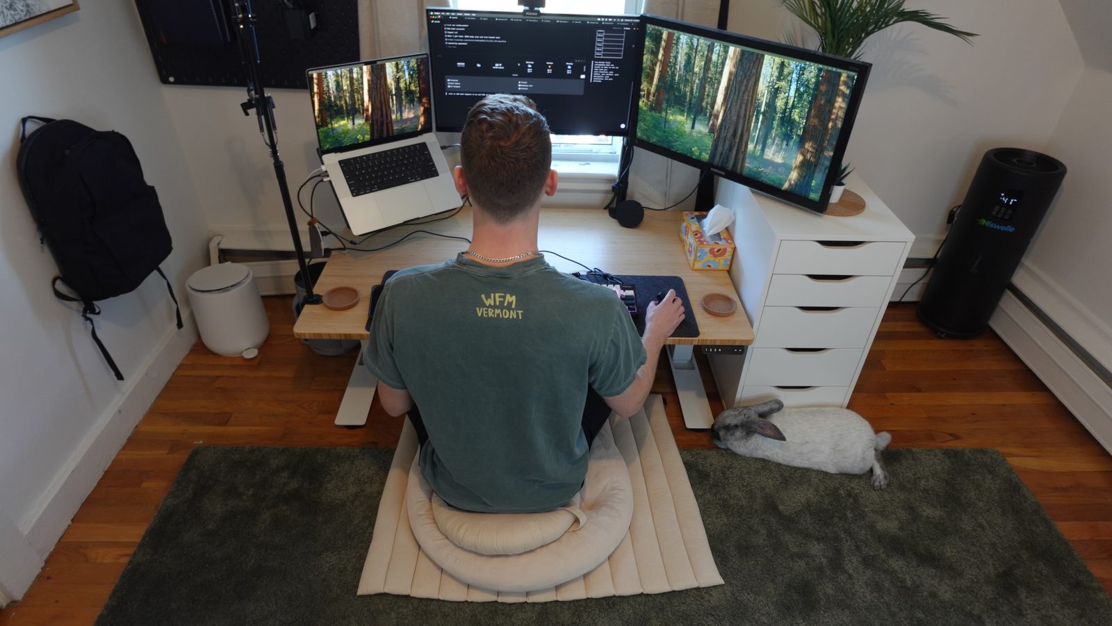 Ryan sitting cross-legged on the Grounded floor cushion at a low desk, a rabbit resting on the rug beside him.